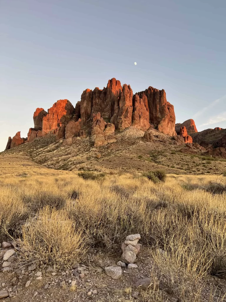 The setting sun reflects off the volcanic rocks of the Superstition Mountains in Arizona, casting an orange glow on the mountain.