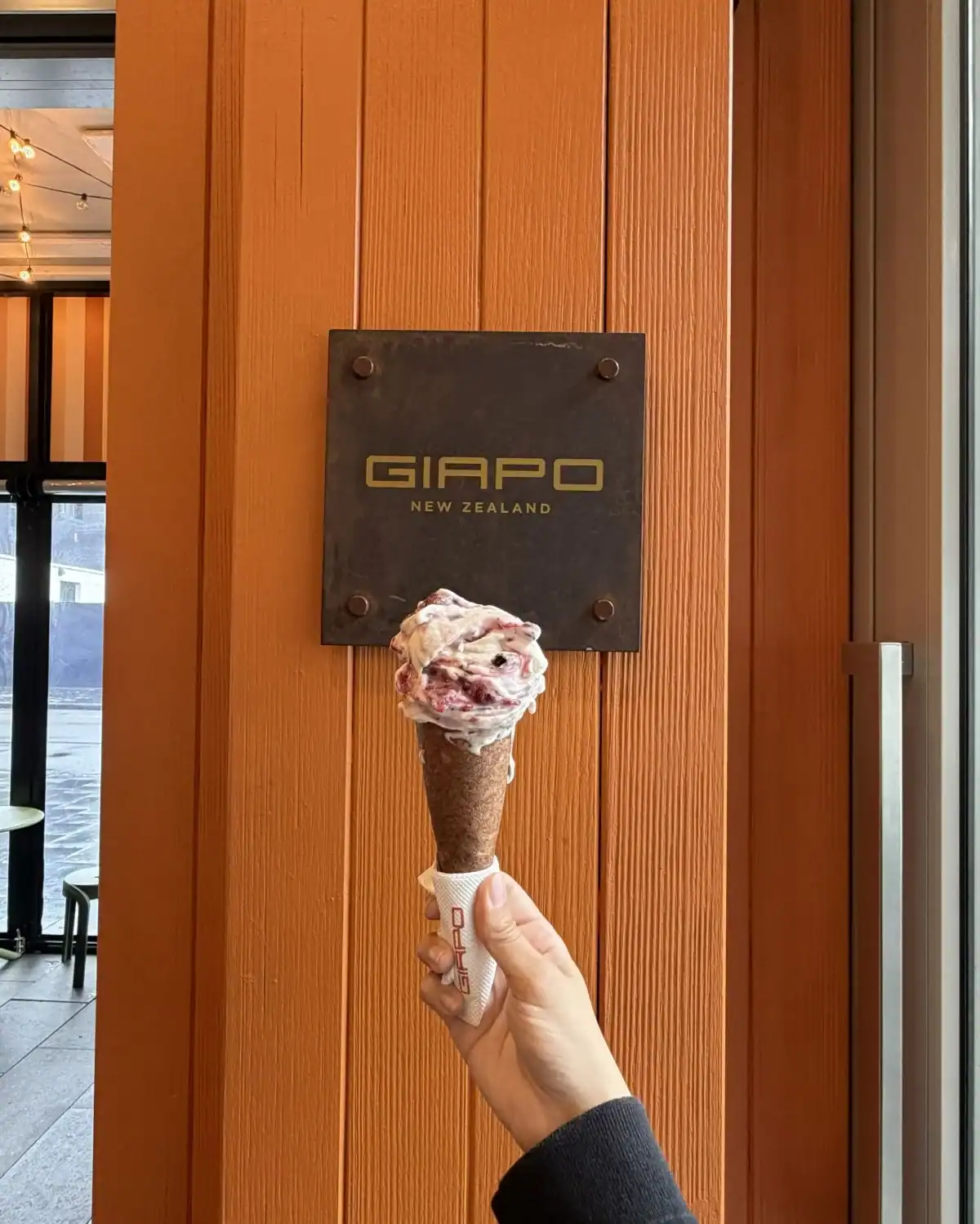 Hand holding a gelato cone in front of a Giapo sign in Auckland, New Zealand.