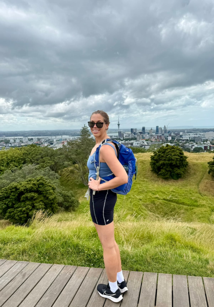 Woman standing on Mount Eden with the Auckland skyline in the background.